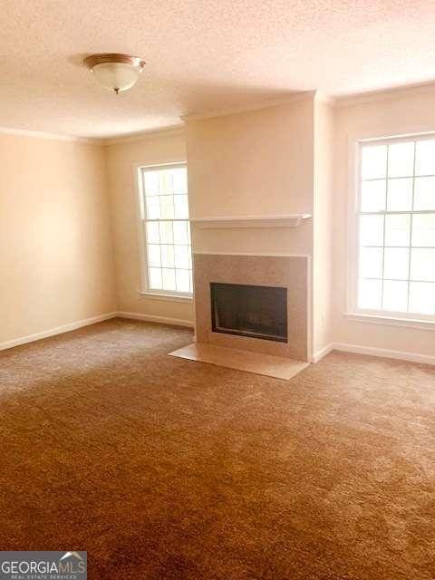 unfurnished living room with carpet floors, a textured ceiling, and crown molding