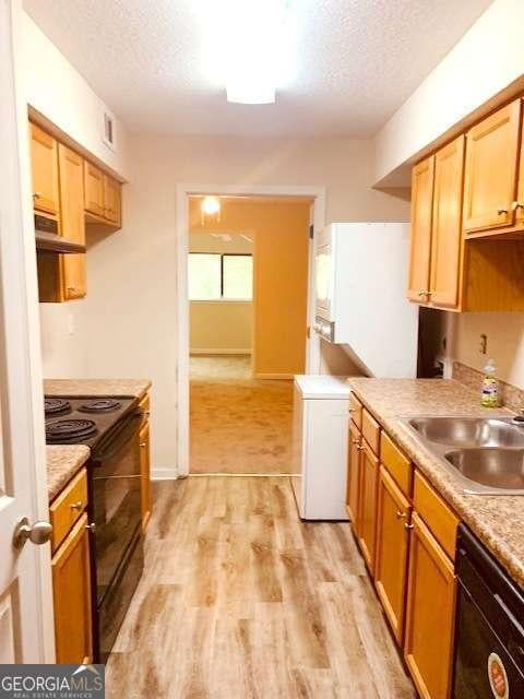 kitchen featuring sink, black appliances, a textured ceiling, and light hardwood / wood-style floors