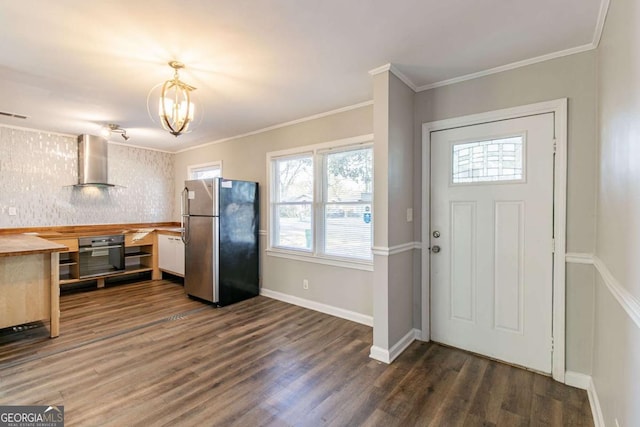 kitchen featuring stainless steel fridge, oven, dark hardwood / wood-style floors, wall chimney range hood, and ornamental molding