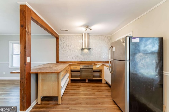 kitchen with wooden counters, wall chimney range hood, ornamental molding, light hardwood / wood-style floors, and stainless steel refrigerator