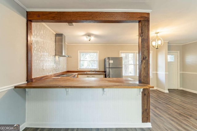 kitchen featuring sink, wall chimney exhaust hood, kitchen peninsula, a breakfast bar area, and stainless steel fridge