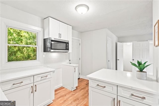 kitchen featuring light hardwood / wood-style floors, a textured ceiling, white cabinets, and tasteful backsplash