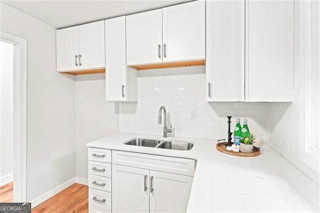 kitchen with light stone countertops, decorative backsplash, sink, light wood-type flooring, and white cabinets