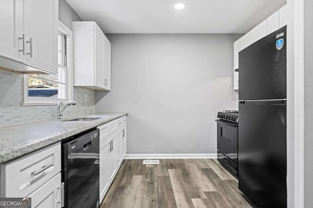 kitchen with sink, backsplash, white cabinets, light stone countertops, and black appliances