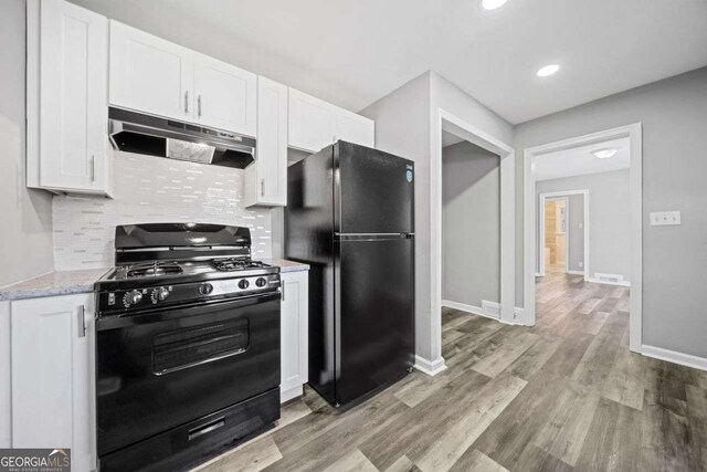 kitchen featuring light stone countertops, black appliances, white cabinetry, decorative backsplash, and light hardwood / wood-style flooring