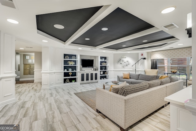 living room featuring built in shelves, a raised ceiling, and decorative columns