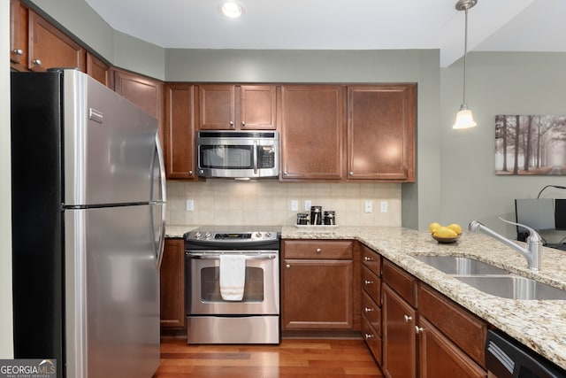 kitchen with sink, wood-type flooring, appliances with stainless steel finishes, pendant lighting, and decorative backsplash