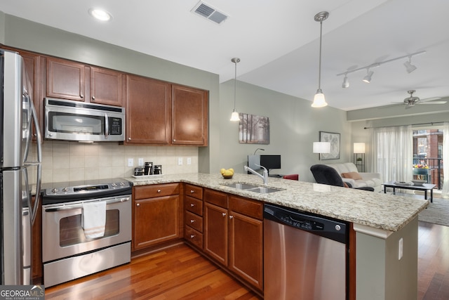 kitchen with appliances with stainless steel finishes, pendant lighting, tasteful backsplash, sink, and kitchen peninsula