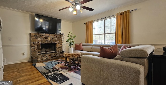 living room with a fireplace, hardwood / wood-style flooring, ornamental molding, ceiling fan, and a textured ceiling