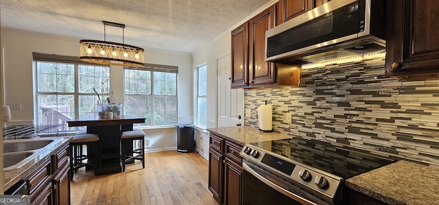 kitchen featuring tasteful backsplash, decorative light fixtures, ornamental molding, appliances with stainless steel finishes, and light stone countertops