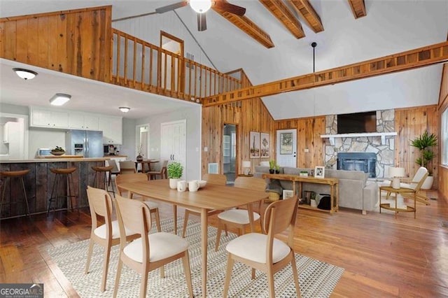 dining room featuring wood-type flooring, wooden walls, beamed ceiling, and high vaulted ceiling