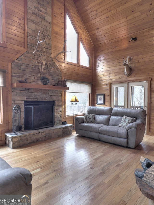 living room featuring high vaulted ceiling, light hardwood / wood-style floors, a stone fireplace, and a healthy amount of sunlight