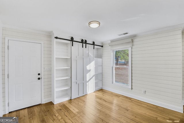 unfurnished room with hardwood / wood-style flooring, a barn door, and crown molding