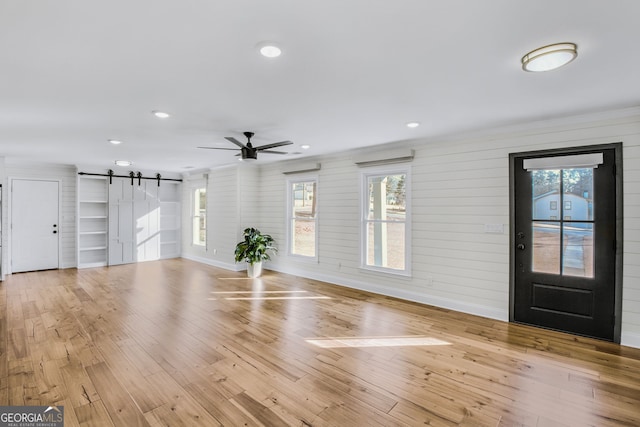 interior space featuring light hardwood / wood-style flooring, ornamental molding, a barn door, and ceiling fan