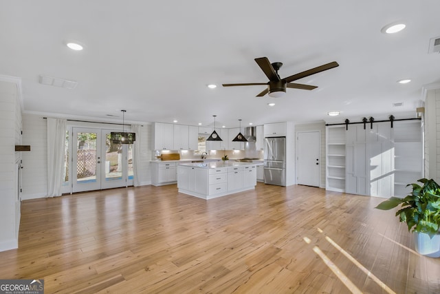 unfurnished living room with sink, light hardwood / wood-style flooring, ceiling fan, a barn door, and french doors