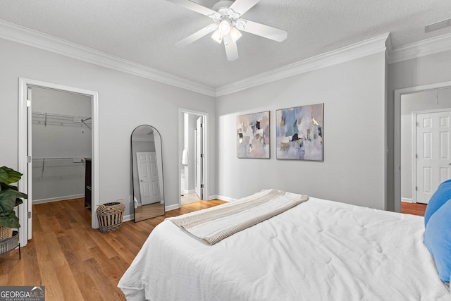 bedroom featuring a walk in closet, ornamental molding, and light wood-type flooring