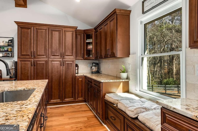 kitchen with sink, tasteful backsplash, light stone counters, light hardwood / wood-style floors, and lofted ceiling