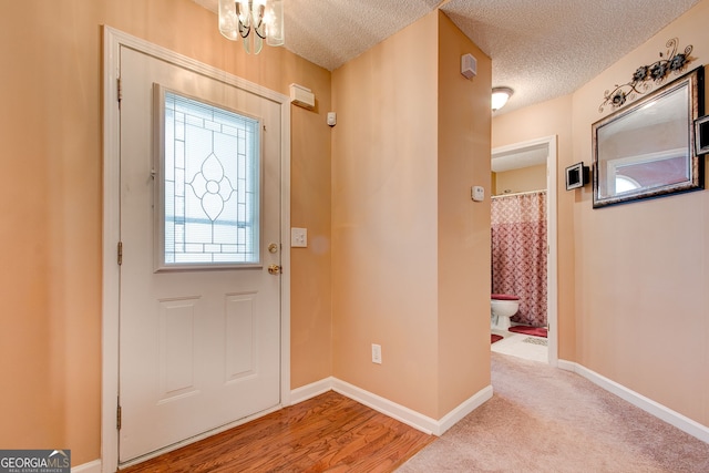 entryway with a textured ceiling, light wood-type flooring, and a chandelier