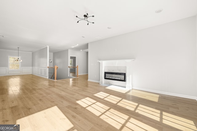 unfurnished living room with an inviting chandelier, light wood-type flooring, and a high end fireplace