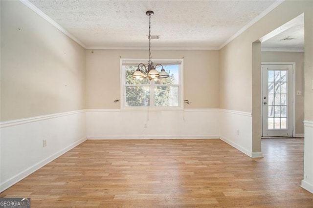 unfurnished dining area with crown molding, light hardwood / wood-style floors, a textured ceiling, and an inviting chandelier