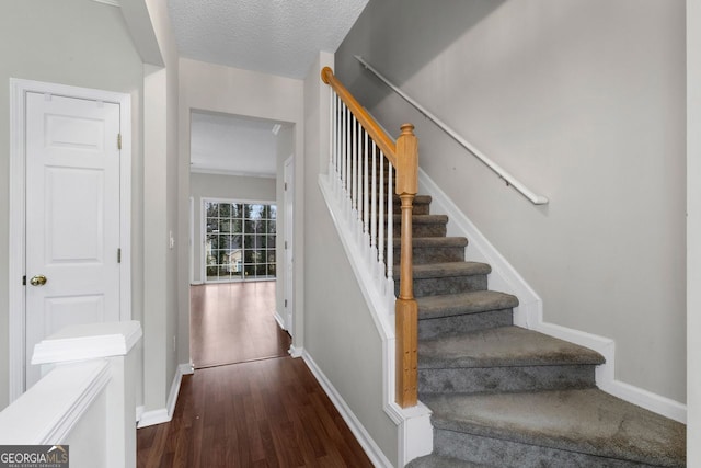 staircase featuring a textured ceiling, baseboards, and wood finished floors