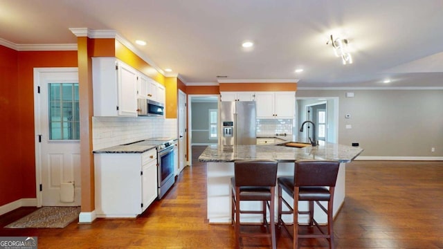 kitchen with white cabinets, appliances with stainless steel finishes, a kitchen bar, sink, and a kitchen island with sink