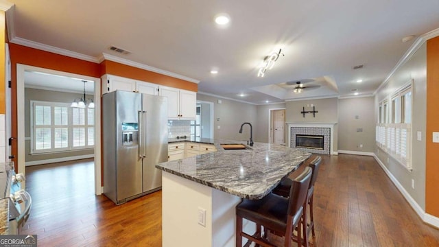 kitchen featuring a kitchen breakfast bar, sink, a tiled fireplace, white cabinets, and high quality fridge