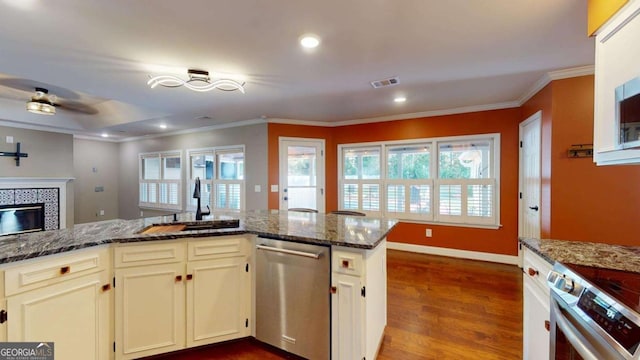 kitchen with appliances with stainless steel finishes, hardwood / wood-style flooring, sink, dark stone countertops, and a tiled fireplace