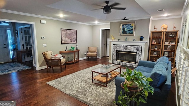 living room featuring dark wood-type flooring, a tray ceiling, a tile fireplace, and ornamental molding