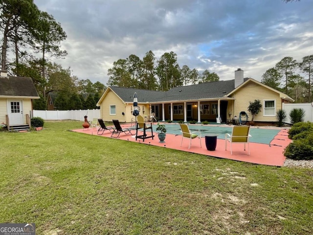 rear view of house featuring a patio area, a covered pool, a lawn, and an outdoor structure