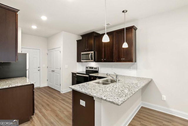 kitchen with light stone countertops, stainless steel appliances, sink, hanging light fixtures, and light wood-type flooring