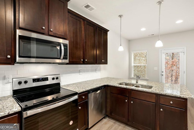 kitchen with sink, kitchen peninsula, pendant lighting, stainless steel appliances, and light stone counters