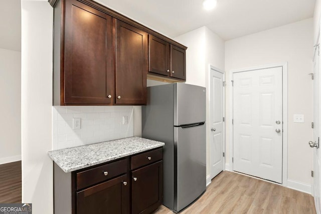 kitchen with stainless steel fridge, backsplash, light wood-type flooring, light stone counters, and dark brown cabinetry