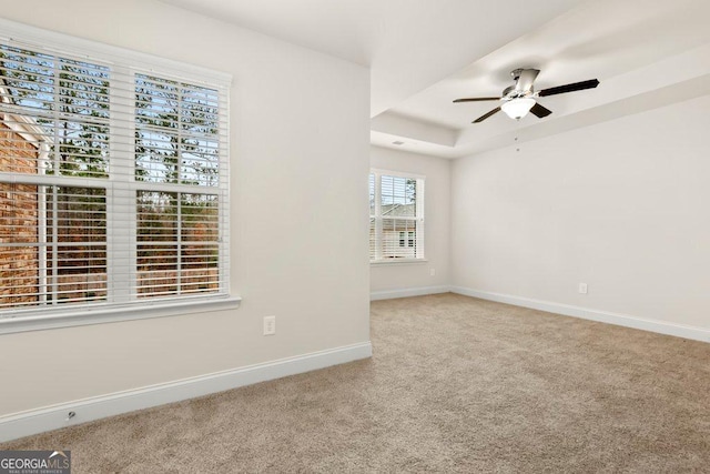 empty room with ceiling fan, carpet floors, and a raised ceiling