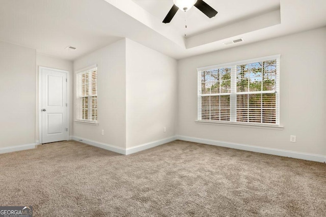 carpeted empty room featuring plenty of natural light, ceiling fan, and a raised ceiling