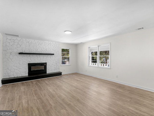 unfurnished living room with light hardwood / wood-style floors and a stone fireplace