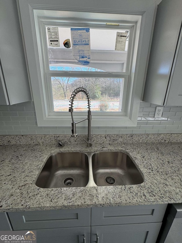 interior details featuring sink, light stone counters, decorative backsplash, and gray cabinets