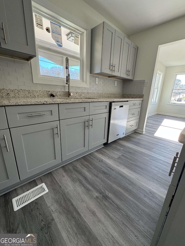 kitchen with light stone countertops, dishwasher, dark hardwood / wood-style flooring, decorative backsplash, and gray cabinetry