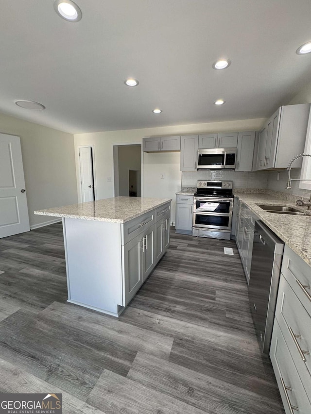 kitchen featuring a center island, light stone countertops, sink, stainless steel appliances, and gray cabinets