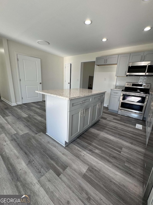 kitchen with tasteful backsplash, gray cabinetry, light stone counters, a kitchen island, and stainless steel appliances