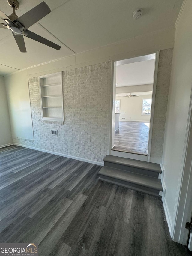 empty room with ceiling fan, brick wall, dark hardwood / wood-style floors, and built in features