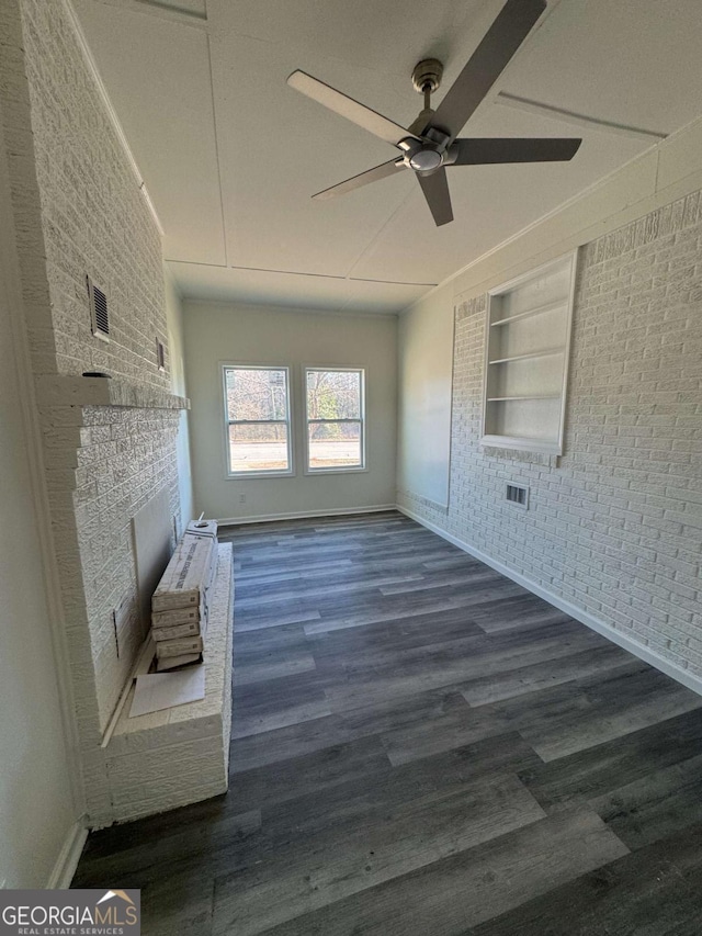 unfurnished living room with ceiling fan, dark hardwood / wood-style flooring, built in shelves, a fireplace, and brick wall