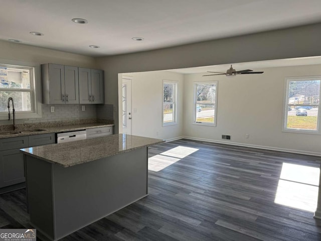 kitchen with light stone countertops, a center island, sink, dark hardwood / wood-style floors, and white dishwasher