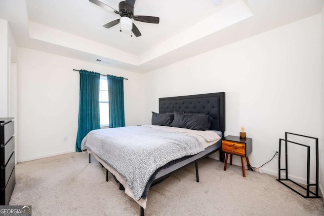 carpeted bedroom with ceiling fan and a tray ceiling