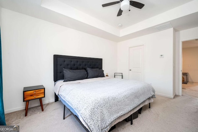 bedroom featuring ceiling fan, light colored carpet, and a tray ceiling