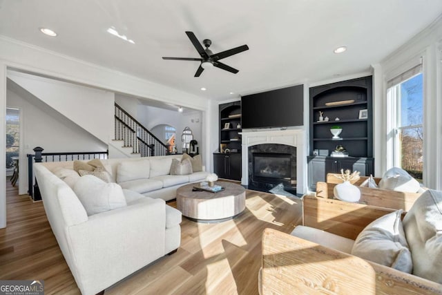 living room with a high end fireplace, hardwood / wood-style floors, ornamental molding, built in features, and ceiling fan