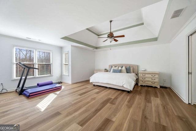 bedroom featuring ceiling fan, crown molding, light hardwood / wood-style floors, and a tray ceiling