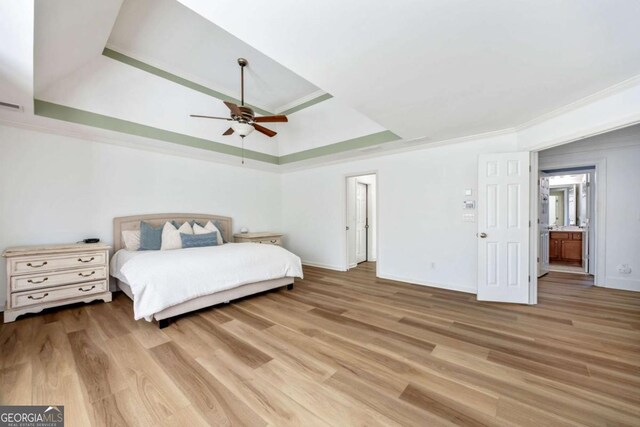 bedroom with light hardwood / wood-style flooring, ceiling fan, a raised ceiling, ornamental molding, and connected bathroom