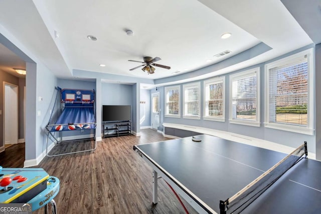 playroom with ceiling fan, dark hardwood / wood-style floors, and a tray ceiling