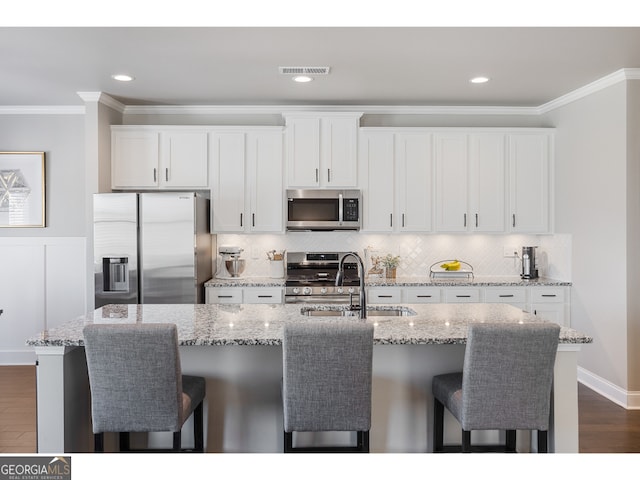 kitchen featuring appliances with stainless steel finishes, a kitchen island with sink, white cabinets, sink, and light stone counters